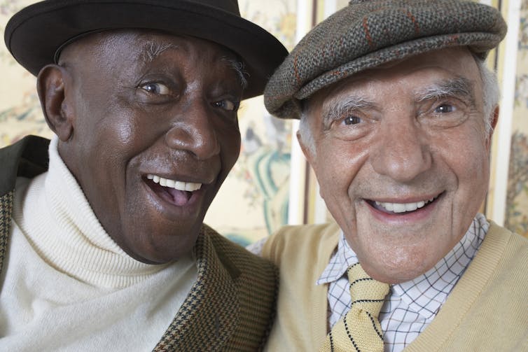 Two dapper older men smiling with their arms around each other, one Black and one white.
