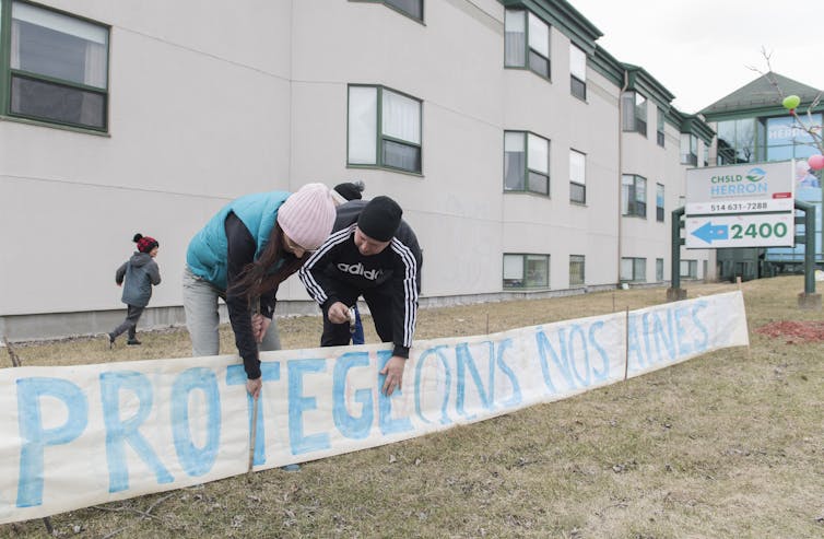 People stand outside a long term care home next to a long banner.