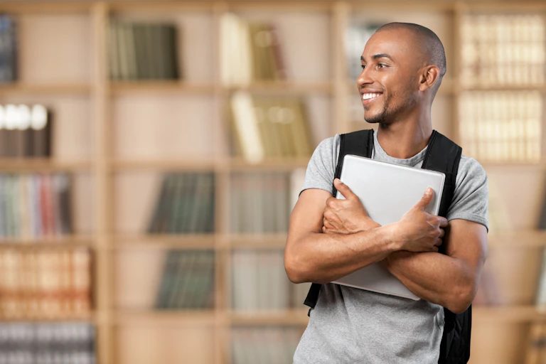 Smiling young man holding laptop in library