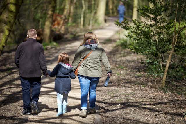 A child walks on a track with her parents, holding hands.