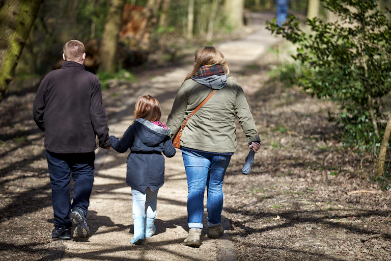 A child walks on a track with her parents, holding hands.