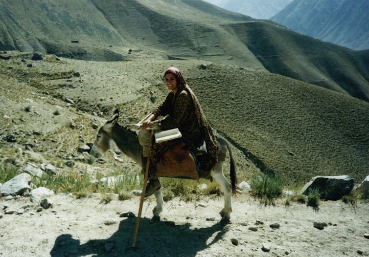 Uma mulher montada em um burro em um cenário montanhoso
