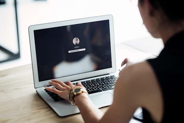A woman types a password on a laptop.