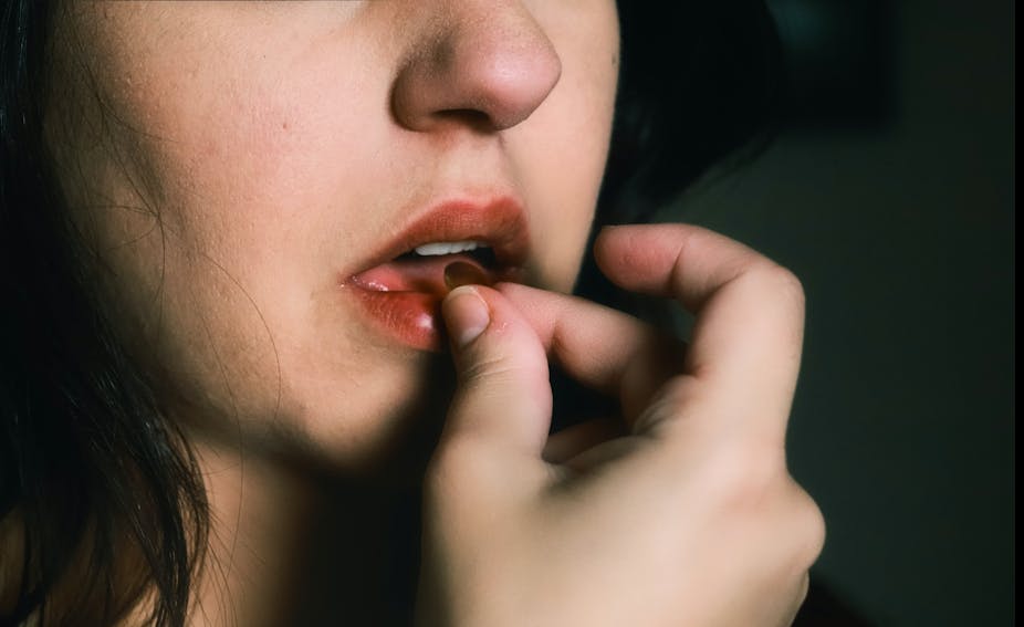 Une jeune femme dont le visage est partiellement masqué met une pilule dans sa bouche.