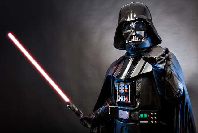 Photo of a Darth Vader costume replica with one arm outstretched and the other holding a lightsaber