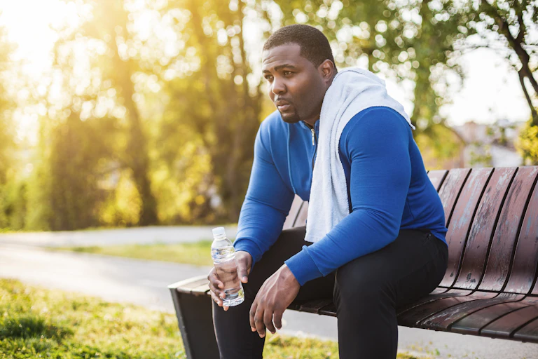 Man exhausted after his workout sits on a park bench with a bottle of water.