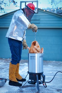 A man in a bomber jacket places a turkey in a deep fryer.