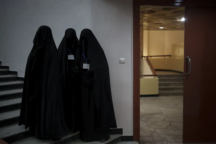 Trois femmes vêtues de noir et voilées debout devant une porte