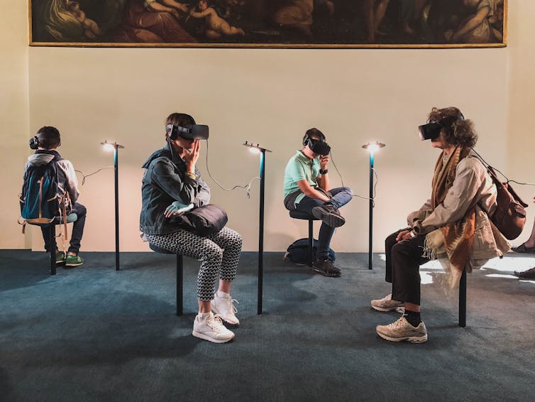 Four people wearing VR headsets perched on stools