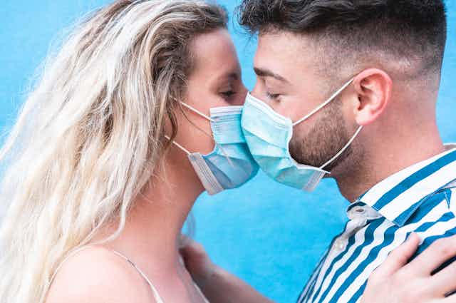 A young couple kiss while wearing COVID-19 masks.