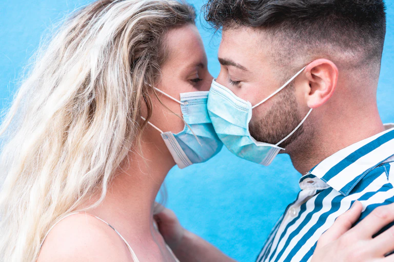A young couple kiss while wearing COVID-19 masks.