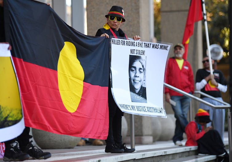 A person stands with an Aboriginal flag and a picture of Elijah Doughty outside the supreme court.