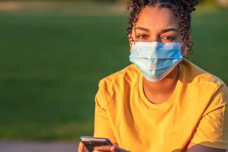 Teen in a mask holds a phone.