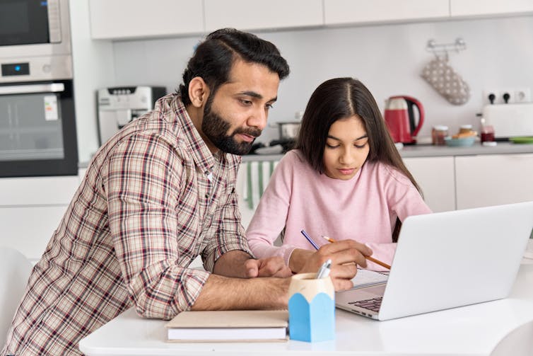 Father and daughter look at a laptop together.