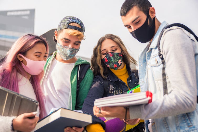 Four older teens in masks look down at a notebook.