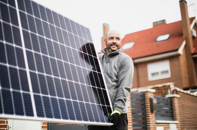 A man carries a solar panel for a roof installation