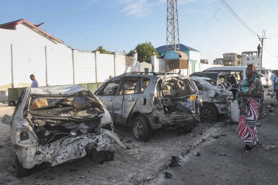 A woman walks in front of vehicles marred by explosions in Somalia