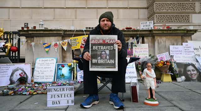 Richard Ratcliffe, on day 19 of his hunger strike, sits outside the foreign office holding up the front cover of a newspaper with a story about his wife Nazanin Zaghari-Ratcliffe who is detained in Iran.