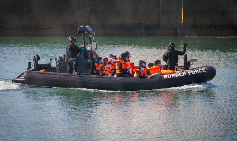 A border force lifeboat carrying a group of people in orange life jackets to shore