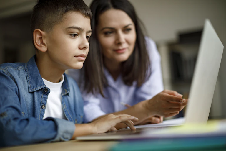 A mother and son look at a laptop screen together.