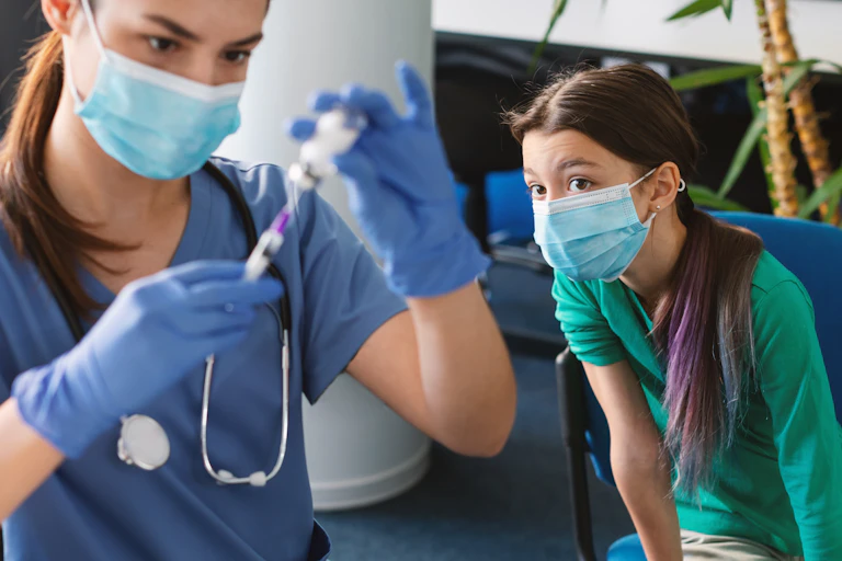 Une jeune adolescente regarde la soignante préparer son injection.