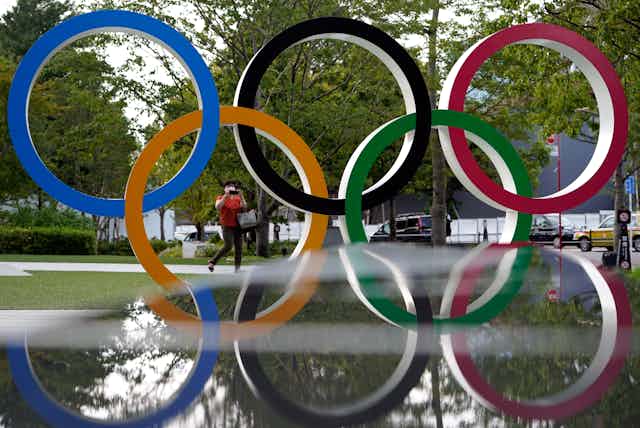 The Olympic Rings are seen against a green leafy background.
