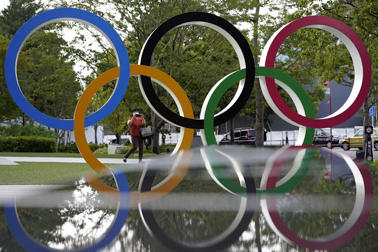 The Olympic Rings are seen against a green leafy background.