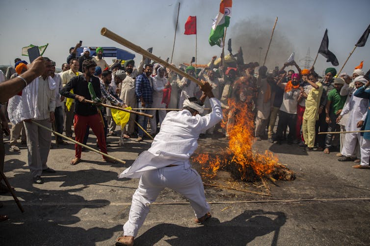 Indian man with baseball bat hitting burning effigy.
