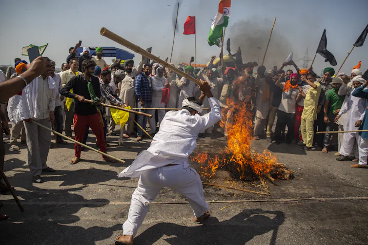 Indian man with baseball bat hitting burning effigy.