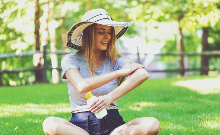 Woman wearing hat putting on sunscreen