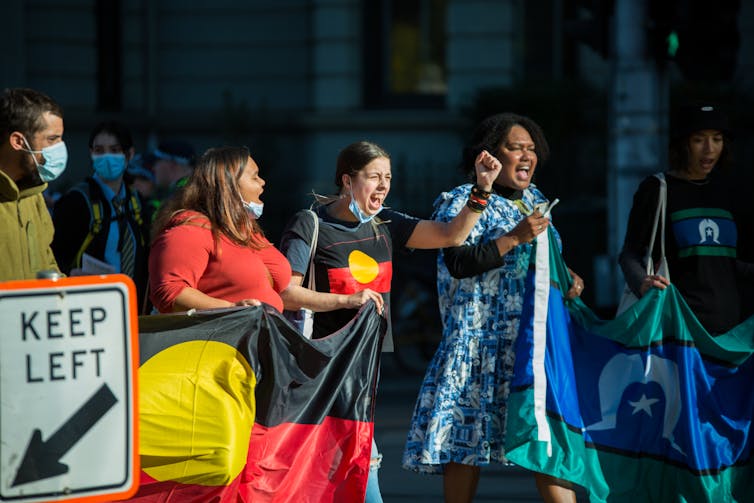 People hold the Aboriginal and Torres Strait Islander flags while protesting.