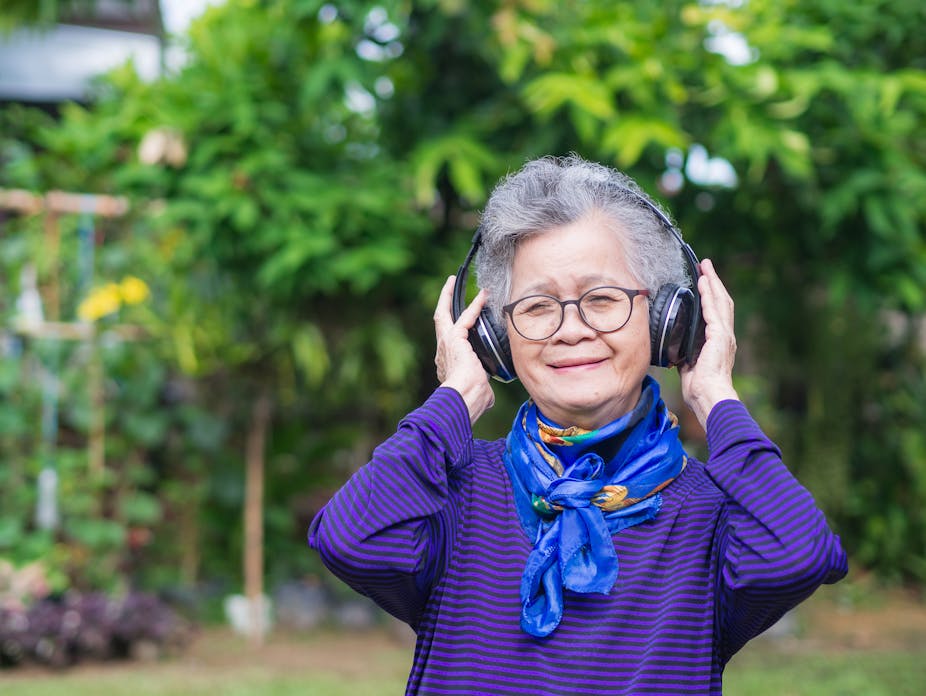 Older woman smiles as she listens to music with wireless headphones outdoors.