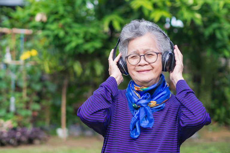 Older woman smiles as she listens to music with wireless headphones outdoors.