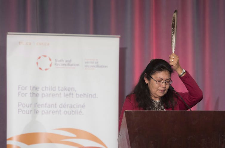 A woman holds an eagle feather above her head in front of a copy of a report.