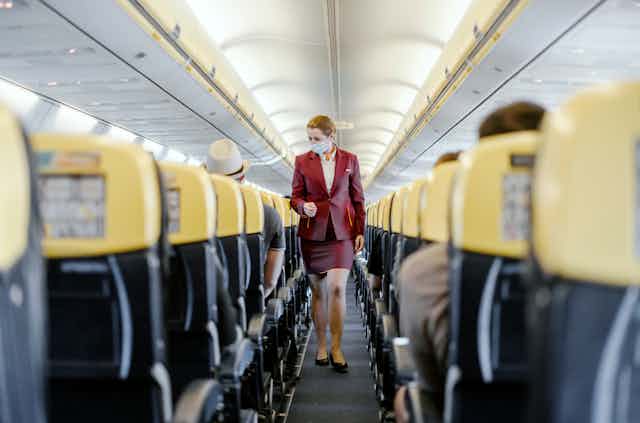A flight attendant wearing a face mask walks down the aisle of a nearly empty Ryanair flight