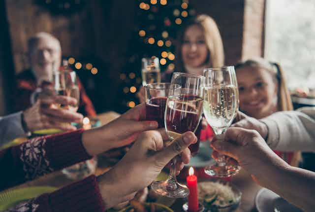 People wearing holiday sweaters clink champagne glasses
