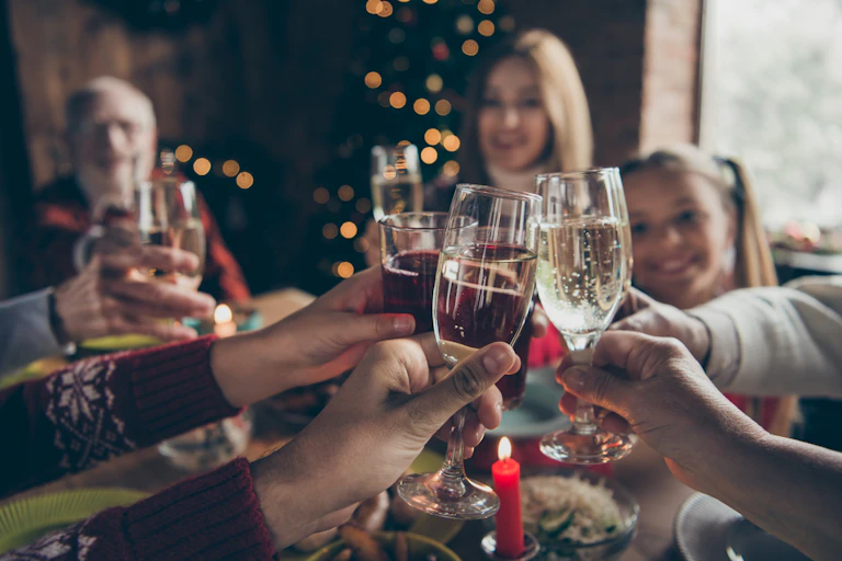 People wearing holiday sweaters clink champagne glasses