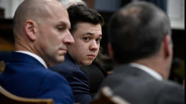 Kyle Rittenhouse looks back towards a camera while flanked by his defense attorneys.