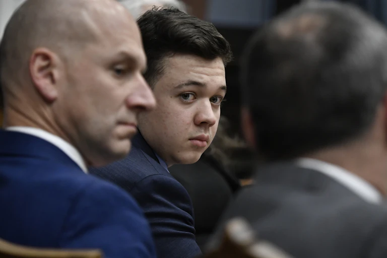 Kyle Rittenhouse looks back towards a camera while flanked by his defense attorneys.