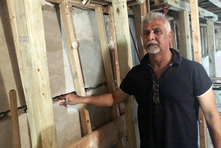 Man stands next to foundation wall with large crack.