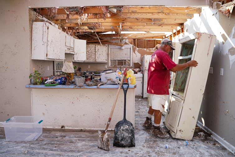 A man moves cabinet in a kitchen with a missing roof and walls splattered with mud from the storm. Grand Isle, La.