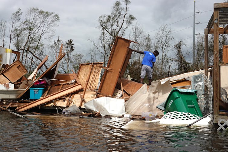 A young man walks through furniture and household items strewn about by the hurricane, rescuing his mother's belongings.