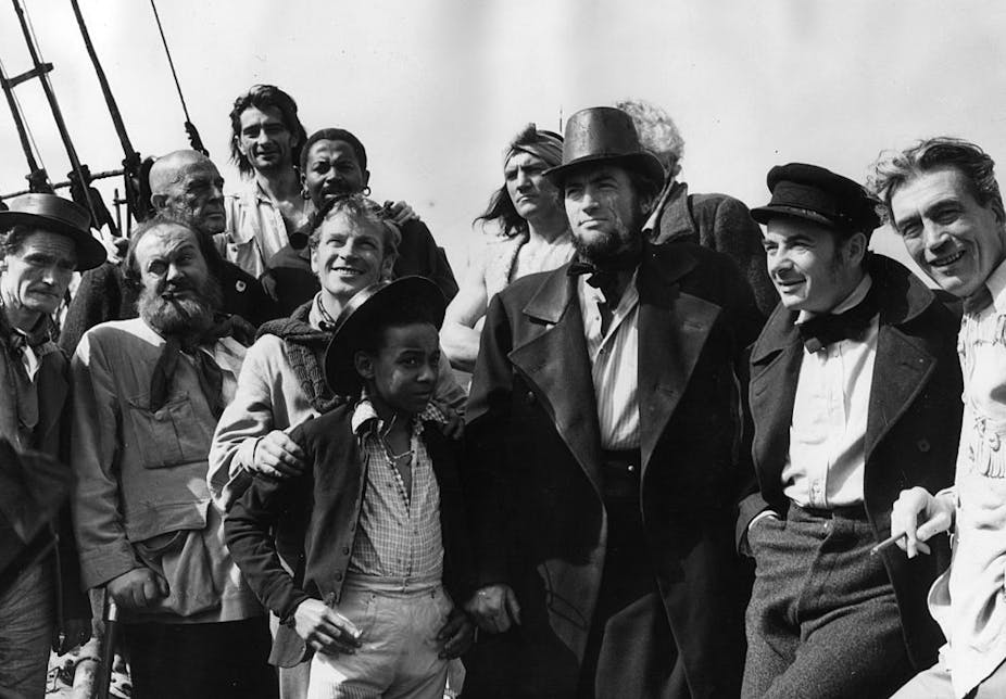 A black and white photograph shows a group of men dressed as 19th century sailors.