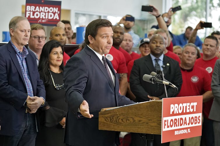 Man stands at podium surrounded by supporters.