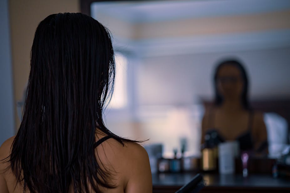 Young person with long hair looks at blurry reflection in mirror