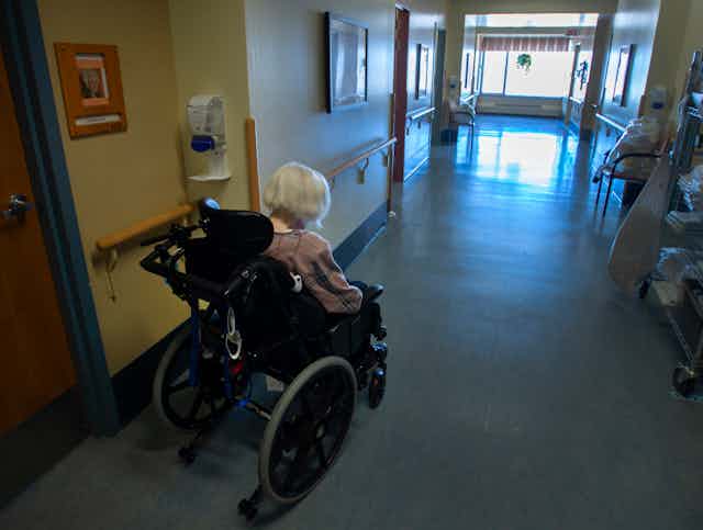 Une dame âgée en fauteuil roulant dans un corridor.