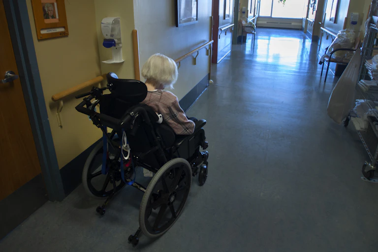 Une dame âgée en fauteuil roulant dans un corridor.