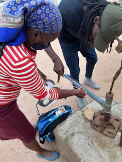 A man and a woman use a long thin plastic pipe to measure water in a well