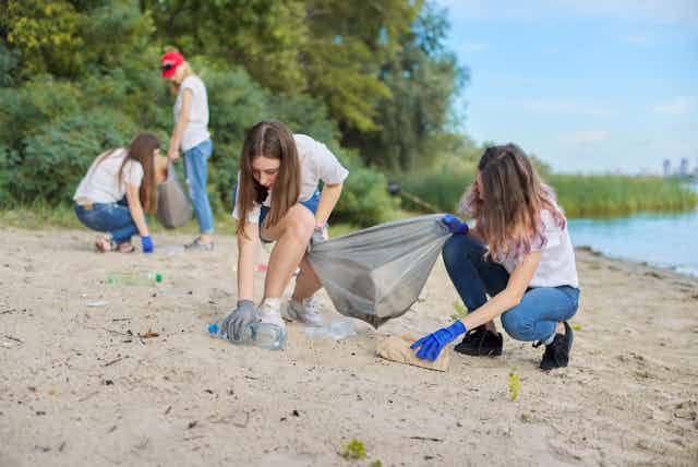 Chicas adolescentes recogiendo basura en una playa.