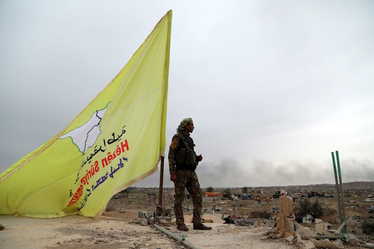 A fighter with Syrian Democratic Forces (SDF) next to an SDF flag in Baghuz, where a US airstrike killed more than 70 civilians in March 2019.